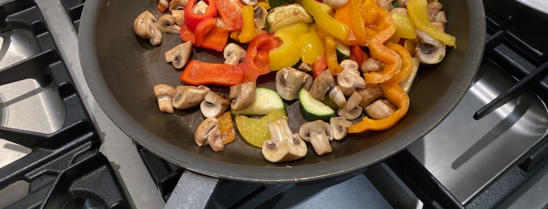 Mushroom, Peppers, Tomatoes and Zucchini are cooking in a pan on a stovetop.